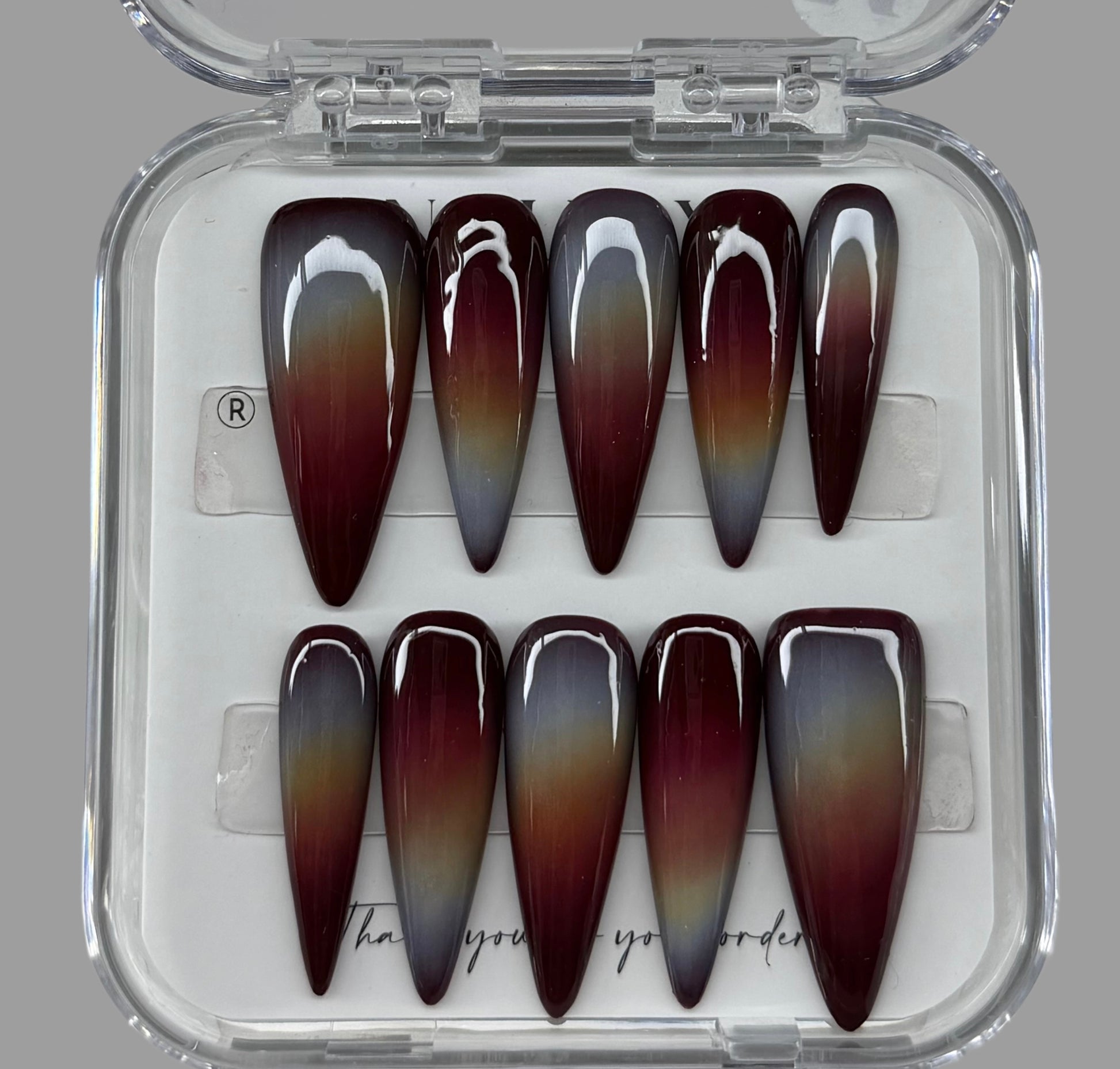 Set of gradient nail art designs in a clear case on a gray background