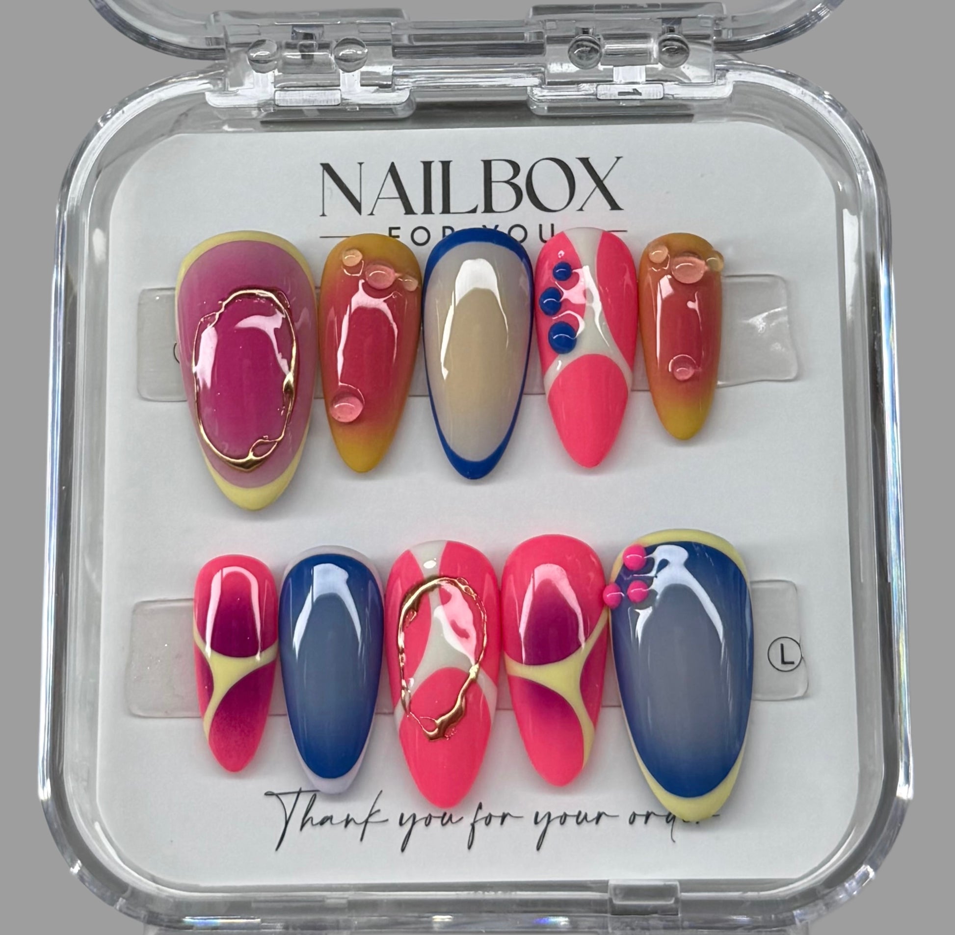 Set of colorful nail designs in a clear 'Nailbox' case on a gray background